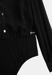 Sorte bodysuit med lange ærmer, med gyldne trykknapper og samlet tekstur ved taljen. Logo "Guess" i guld på hoften.