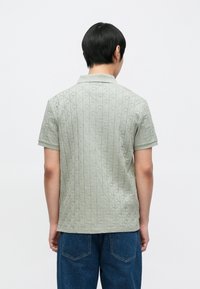 �Κοντομάνικο πόλο σε ανοιχτό πράσινο με υφή διαμαντένιου μοτίβου, με κλασικό γιακά και ίσια τελείωμα. Φορεμένο με μπλε τζιν.