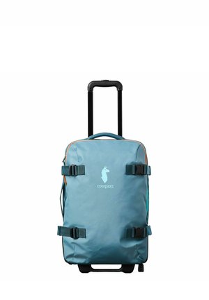Maleta de mano azul con ruedas, asa retráctil, correas de compresión y logo blanco de llama con texto "cotopaxi" en la parte frontal.