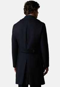 Námořnický vlněný kabát s upraveným střihem, se zadním rozparkem, opaskem v pase a knoflíkovými detaily. Hladká textura a strukturovaný design.