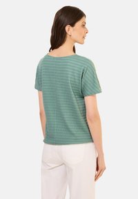 Tričko s krátkým rukávem v mátově zelené barvě s texturovaným, žebrovaným vzorem. Přímý střih a kulatý výstřih, spárované s světle zbarvenými kalhotami.