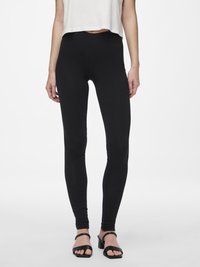 Sorte leggings laget av elastisk stoff, med høy midje og tett passform, kombinert med sorte sandalletter.