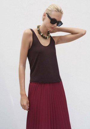 Top nero senza maniche abbinato a una gonna plissè bordeaux. Il modello indossa una collana di perline spesse e occhiali da sole scuri. Tessuto con una superficie liscia.