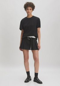 Zwarte t-shirt met korte mouwen gecombineerd met een zwarte plissérok. Bevat een riem met een gesp, zwarte sokken en glanzende instappers.