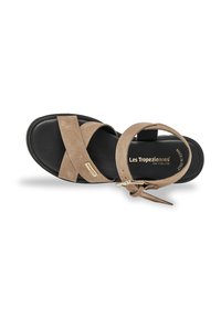 Sandal de ante beige con correas cruzadas, suela negra, correa ajustable en el tobillo y detalles en dorado. Perfil plano, diseño minimalista.