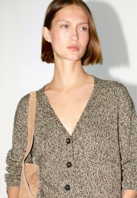 Brązowy dziergany kardigan z głębokim dekoltem w literę V, z trzema guzikami i długimi rękawami, w połączeniu z jasnobrązową torebką na ramię.