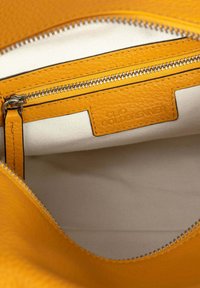 Geel lederen interieur met ritszak en witte stoffen voering; bevat gestructureerd materiaal en een merketiket. Rits is zilverkleurig.