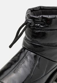 Botte d'hiver noire brillante avec fermeture à cordon réglable et col rembourré, présentant un matériau synthétique texturé et des détails de couture.