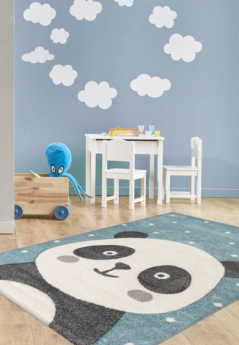 Panda-Themen-Teppich mit einem grauen Panda-Gesicht auf einem blauen Hintergrund mit weißen Punkten. Der Teppich hat eine plüschige Textur und abgerundete Kanten.