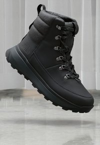 Czarne buty trekkingowe z wyściełanym kołnierzem, metalowymi oczkami, teksturowanymi akcentami z tkaniny oraz wytrzymałą podeszwą, zaprojektowane z myślą o trwałości i przyczepności.