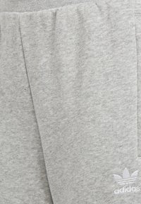 Grå bomullssweatpants med en texturerad yta, med en plissédesign och en vit Adidas-logga på nedre vänstra sidan.