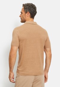Beige poloshirt met korte mouwen, een klassieke kraag, een zachte textuur en zijsplits, weergegeven vanuit een achterhoek.