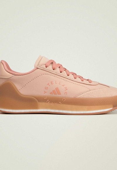 Light pink athletic shoe featuring a synthetic upper, padded collar, textured accents, and a translucent rubber sole with a slight curve.