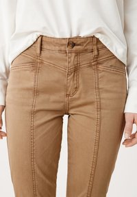 Braune hochgeschnittene Hose mit taillierter Passform, strukturiertem Stoff und vertikalen Steppnähten entlang der Vordernaht.