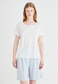 Haut blanc à manches courtes avec un col rond et des poignets retroussés, fabriqué en tissu lisse. Associé à un short en lin bleu clair, ample.