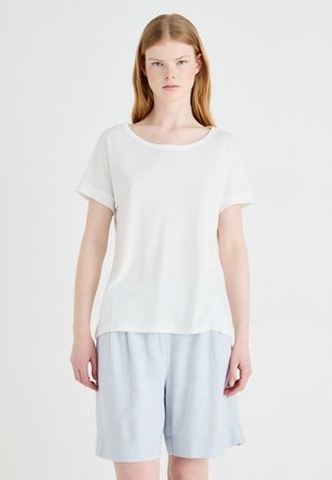 White short-sleeve top with a round neckline and rolled cuffs, made of smooth fabric. Paired with light blue, loose-fitting linen shorts.