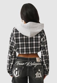 Przycięta, czarno-biała bluza w kratkę z szarym kapturem, w zestawie z ciemnymi dżinsami z białymi haftowanymi akcentami i kieszeniami.