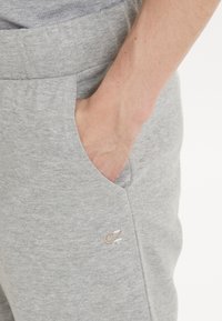 Graue Jogginghose mit weichem Material, elastischem Bund, Seitentaschen und einem kleinen gestickten Logo in einer kontrastierenden Farbe auf der Vorderseite.