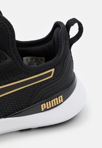Schwarze Mesh-Sportschuhe mit goldenen Akzentstreifen und Branding. Verfügt über eine gepolsterte Sohle und eine strukturierte Oberfläche für Unterstützung und Grip.