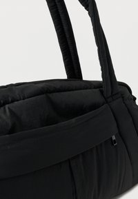 Μαύρη τσάντα χειρός με επένδυση, στρογγυλεμένες λαβές και μπροστινή τσέπη με φερμουάρ, εμφανιζόμενη σε απλό λευκό φόντο.