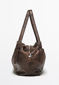 Brun læderhåndtaske med en tekstureret overflade, dobbelte stropper og en central lynlås. Kompakt rund form med synlige syningsdetaljer.