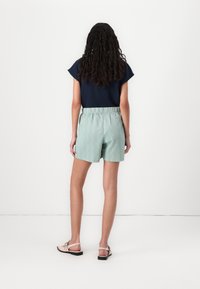 Shorts vert clair avec un motif en zigzag et une taille élastique, associés à un haut bleu marine foncé et des sandales plates.
