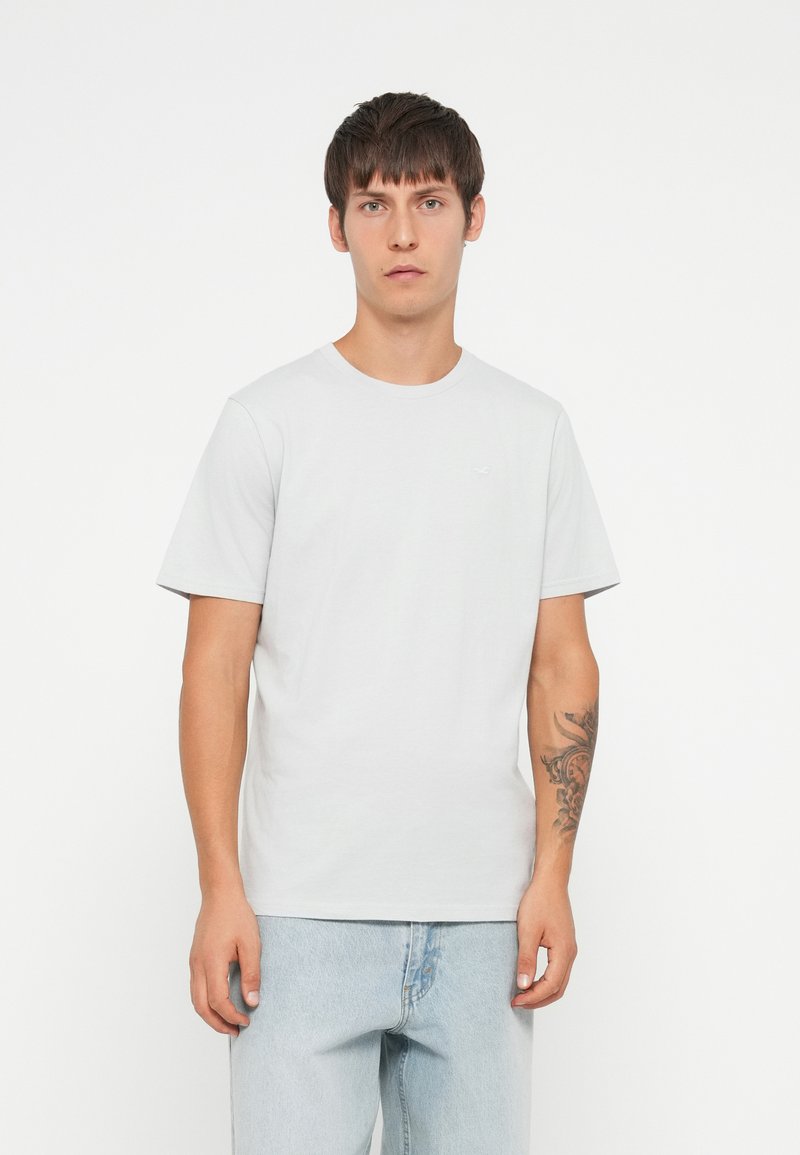 T-shirt in cotone grigio chiaro con maniche corte, colletto tondo e un piccolo logo sul petto. Abbinata a jeans in denim blu chiaro.