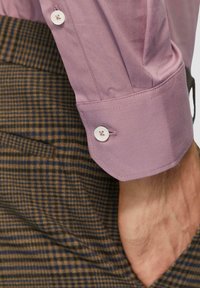 Lichtpaarse katoenen shirtmanchet met een knoop, gecombineerd met een bruine geruite stof eronder. Soepele textuur en op maat gemaakt ontwerp.