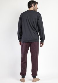 Conjunto de ropa de estar por casa para hombre que incluye una camiseta de manga larga negra y pantalones rojos con estampado y puños. Tejido suave, corte relajado y diseño sencillo.