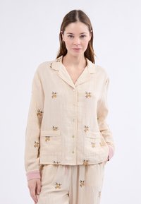 Conjunto de pijama crema con puños rosa claro y patrón a rayas. Presenta bordado floral y dos bolsillos delanteros en la camiseta. Textura suave.