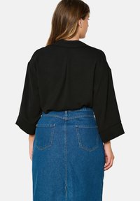 Black long-sleeve top with a relaxed fit, paired with a blue denim skirt featuring two back pockets and a front slit.