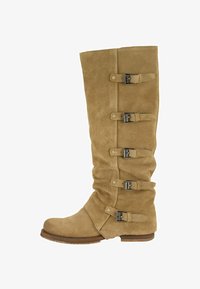 Bota alta hasta la rodilla de ante color canela con cinco correas ajustables con hebillas y un tacón bajo de madera.