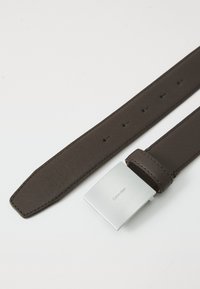 Brun skinnbelte med en jevn finish, med en firkantet sølvfarget metallspenne preget med "Calvin Klein" og flere justeringshull.
