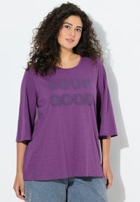 Camiseta ligera de color morado con mangas tres cuartos. Presenta el texto "LUCE BIEN" en gris oscuro. Textura suave y ajuste cómodo. Diseño casual.
