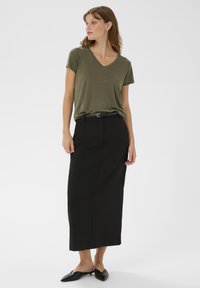 Olive zelené tričko s výstrihom do V v kombinácii s čiernou midi sukňou. Sukňa má elegantný strih a jemný lesk, doplnená čiernymi mule topánkami.