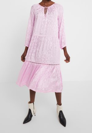 Femme portant une robe midi rose à manches longues avec un motif léopard subtil et une bordure en dentelle, assortie à des bottines noires et blanches.