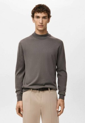 Suéter gris de punto con cuello alto y mangas largas, textura lisa, diseño ajustado, combinado con pantalones beige a medida y un cinturón negro.