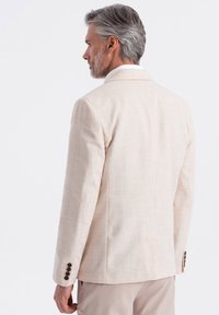 Blazer de lino beige claro con una textura suave, una abertura trasera y cuatro botones oscuros en el puño. Ajuste limpio y entallado.