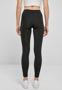 Sorte leggings laget av elastisk stoff med høy midje, tettsittende design og jevn tekstur. Båret med hvite joggesko.