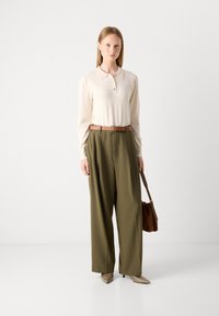 Jasno-beżowa, długorękawowa koszulka polo z guzikami, zestawiona z oliwkowymi spodniami o szerokich nogawkach i brązowym paskiem. Dodatki obejmują brązową torebkę.