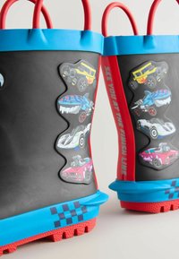 Bottes de pluie en caoutchouc noir avec des accents bleus et rouges. Présentent des graphiques de voitures colorées, deux poignées rouges et un motif à damier sur la semelle.