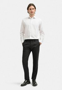 Vit skjorta med lång ärm, kombinerad med svarta byxor och svarta skor. Slätt tyg, skräddarsydd passform och klassiska design detaljer.