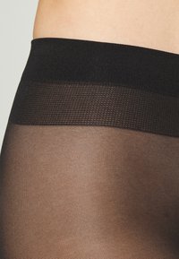 Schwarze, transparente Strumpfhosen mit einer glatten, feinen Textur, einem breiten, einfarbigen schwarzen Bund und einem dezenten Rautenmuster am oberen Teil.