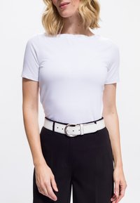 Top bianco a maniche corte con scollatura tonda abbinato a pantaloni neri a vita alta e una cintura bianca con una fibbia circolare in argento.