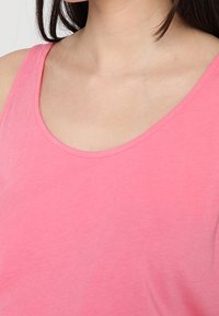 Różowa, bezrękawnikowa bluzka wykonana z gładkiej bawełny. Posiada okrągły dekolt i subtelne detale szwów wzdłuż krawędzi.