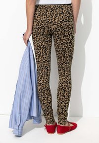 Leggings à imprimé léopard en beige et noir, design ajusté, associés à une chemise rayée bleu clair et des ballerines rouges. Tissu flexible avec une texture lisse.