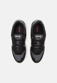 Crne i sive atletske tenisice koje kombiniraju mrežaste i antilop materijale, s teksturiranim detaljima i crvenim Levi's logotipom na jeziku.
