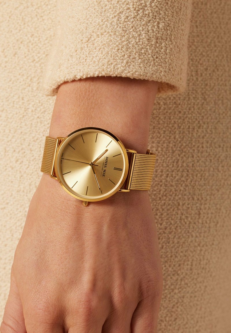 Gold watch with a mesh band, minimalist design, round face, and slender hour markers. Smooth texture; reflective surface.