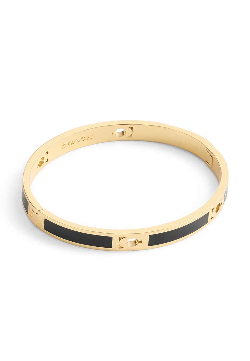 Bracelet en métal doré avec accents en émail noir et détails découpés, portant la marque Coach gravée à l'intérieur.