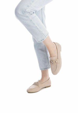 Mocasines de ante beige con suela plana, que cuentan con una correa decorativa y acentos metálicos, combinados con jeans claros de tiro alto y con dobladillo.